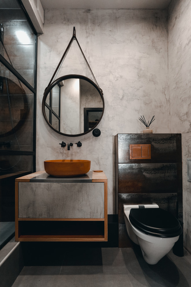 Modelo de cuarto de baño industrial con paredes grises, aseo y ducha, lavabo sobreencimera y suelo gris