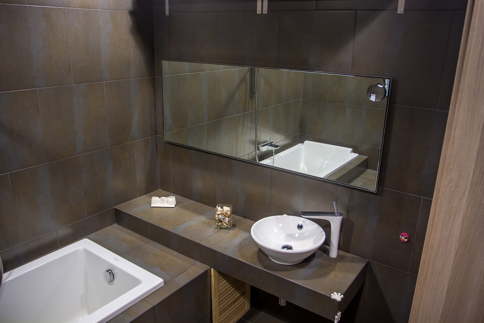 Industriell inredning av ett mellanstort en-suite badrum, med ett platsbyggt badkar, brun kakel, keramikplattor, bruna väggar, klinkergolv i keramik, ett fristående handfat och kaklad bänkskiva