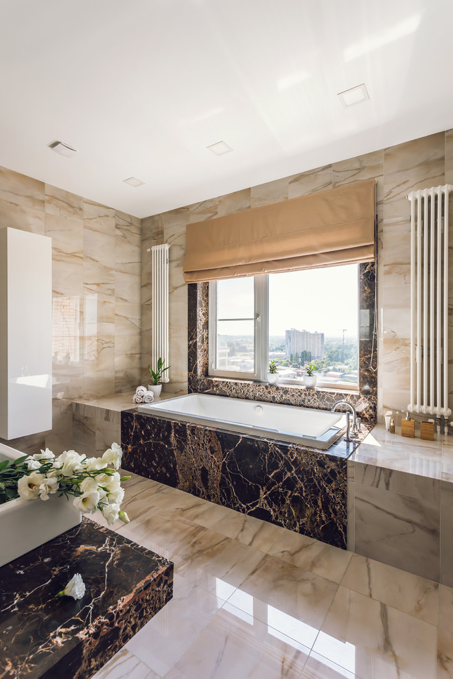 Cette image montre une salle de bain principale design avec une baignoire posée, un carrelage beige, une vasque et un sol beige.