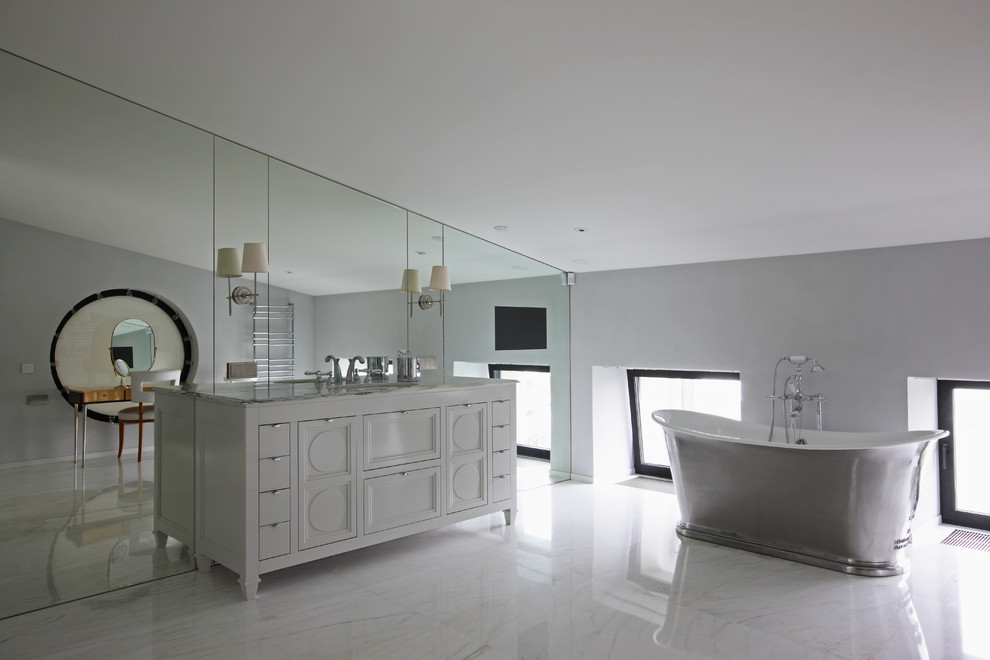 Diseño de cuarto de baño actual grande con puertas de armario blancas, bañera exenta, paredes grises, lavabo bajoencimera y encimera de mármol
