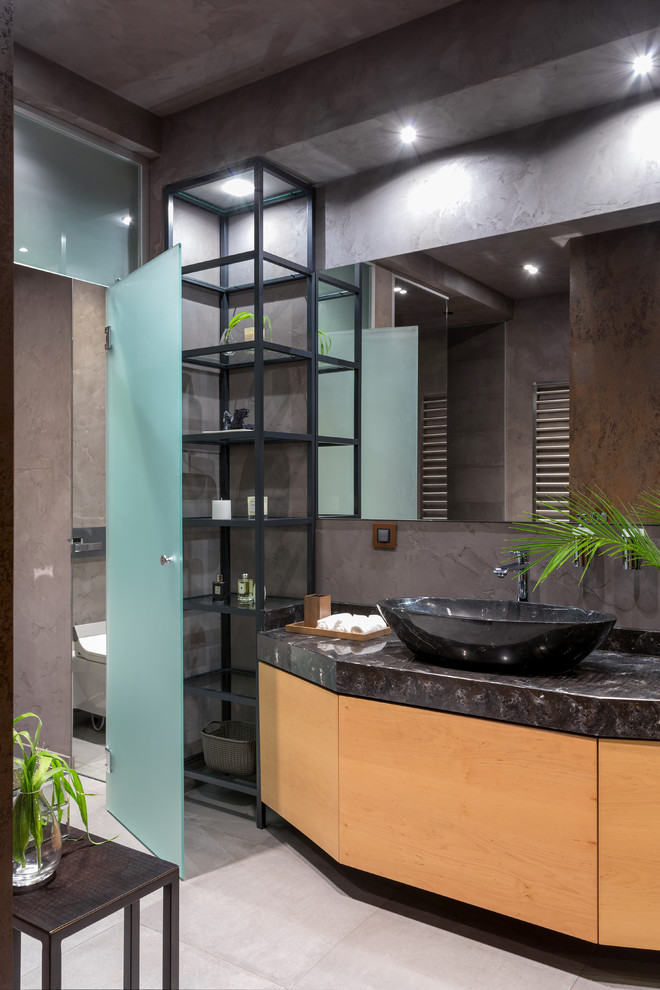 На фото: ванная комната в стиле лофт с плоскими фасадами, фасадами цвета дерева среднего тона, настольной раковиной, серым полом, черной столешницей и серыми стенами с