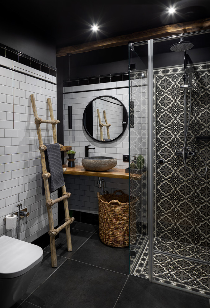 Inredning av ett industriellt litet brun brunt badrum med dusch, med en vägghängd toalettstol, svart och vit kakel, vit kakel, svarta väggar, klinkergolv i porslin, träbänkskiva, svart golv och ett fristående handfat