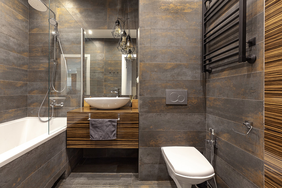 Idéer för funkis brunt badrum med dusch, med släta luckor, skåp i mörkt trä, en vägghängd toalettstol, grå kakel, grått golv, ett badkar i en alkov, en dusch/badkar-kombination, ett fristående handfat, träbänkskiva och med dusch som är öppen