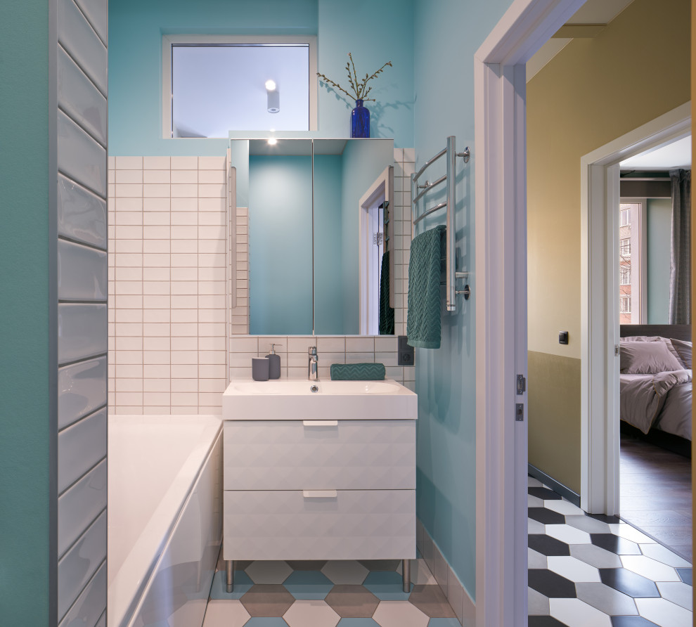 На фото: маленькая ванная комната в современном стиле с плоскими фасадами, белыми фасадами, ванной в нише, душем над ванной, белой плиткой, синими стенами, душевой кабиной, монолитной раковиной, разноцветным полом, открытым душем, белой столешницей, тумбой под одну раковину и напольной тумбой для на участке и в саду