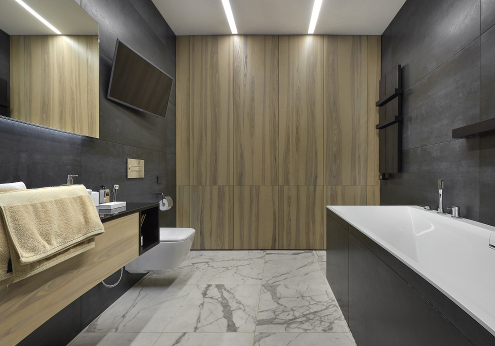 Exemple d'une grande salle de bain principale tendance en bois clair avec un placard à porte plane, une baignoire indépendante, WC suspendus, un carrelage noir, un mur marron, un sol gris, un plan de toilette noir, meuble simple vasque et meuble-lavabo suspendu.