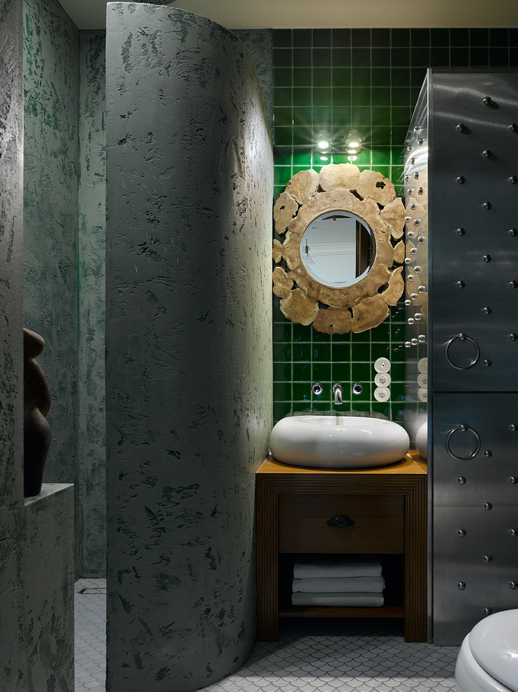 Cette photo montre une salle d'eau éclectique avec un placard à porte plane, des portes de placard marrons, un carrelage vert, une vasque, un sol gris, un plan de toilette marron et un mur vert.