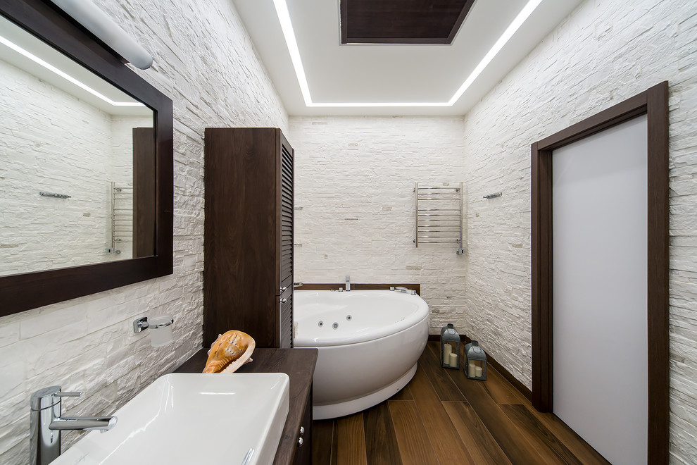 Idéer för stora medelhavsstil brunt en-suite badrum, med luckor med lamellpanel, bruna skåp, ett hörnbadkar, en vägghängd toalettstol, vit kakel, skifferkakel, vita väggar, klinkergolv i porslin, ett nedsänkt handfat, laminatbänkskiva och brunt golv