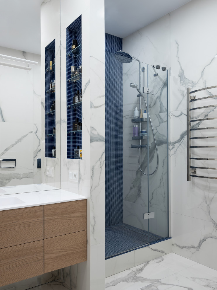 Inredning av ett modernt mellanstort vit vitt badrum med dusch, med släta luckor, skåp i ljust trä, en dusch i en alkov, grå kakel, porslinskakel, klinkergolv i porslin, ett integrerad handfat, grått golv och dusch med gångjärnsdörr