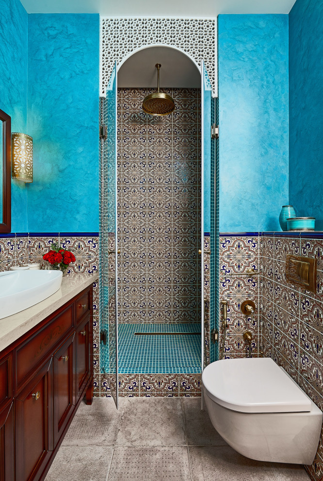 На фото: ванная комната среднего размера в восточном стиле с фасадами с выступающей филенкой, темными деревянными фасадами, душем в нише, инсталляцией, синей плиткой, керамической плиткой, серыми стенами, полом из керамогранита, душевой кабиной, накладной раковиной, столешницей из искусственного камня, серым полом, душем с распашными дверями, бежевой столешницей, сиденьем для душа, тумбой под одну раковину и напольной тумбой с