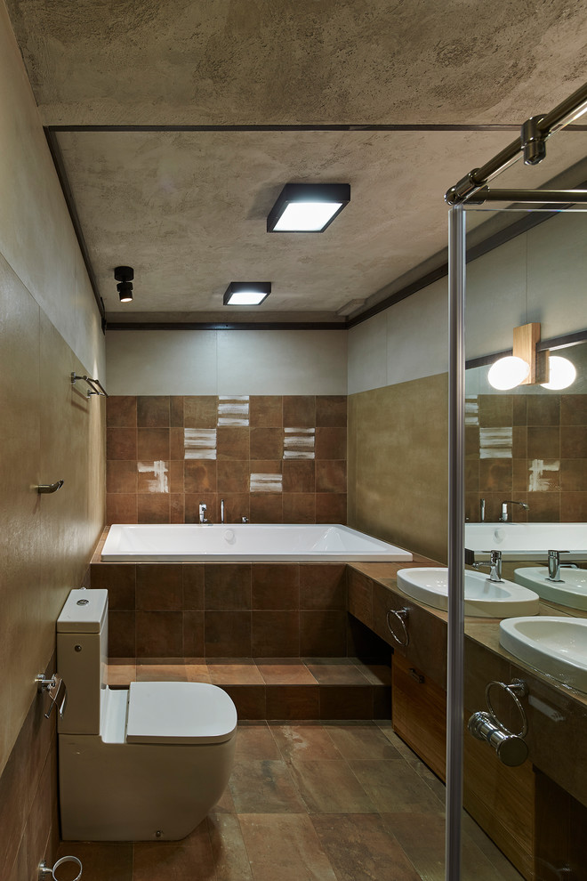Пример оригинального дизайна: главная ванная комната среднего размера в современном стиле с плоскими фасадами, коричневыми фасадами, унитазом-моноблоком, коричневой плиткой, керамогранитной плиткой, серыми стенами, полом из керамогранита, накладной раковиной, столешницей из плитки, коричневым полом и ванной в нише