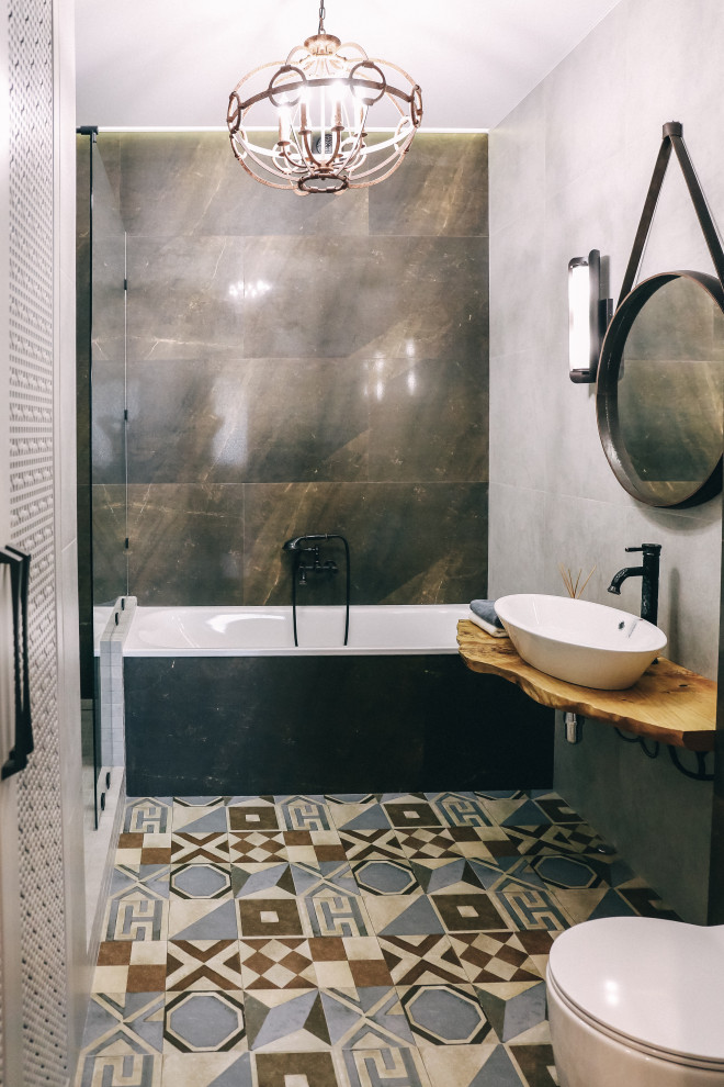 Пример оригинального дизайна: главная ванная комната среднего размера в стиле лофт с ванной в нише, открытым душем, инсталляцией, серой плиткой, керамогранитной плиткой, серыми стенами, полом из керамогранита, накладной раковиной, столешницей из дерева, разноцветным полом, открытым душем, желтой столешницей, тумбой под одну раковину и подвесной тумбой