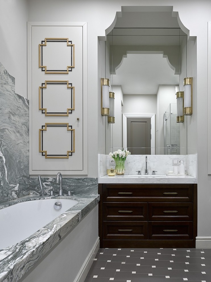 Стильный дизайн: главная ванная комната в стиле неоклассика (современная классика) с темными деревянными фасадами, полновстраиваемой ванной, серой плиткой, белыми стенами, врезной раковиной, серым полом, белой столешницей, мраморной плиткой и зеркалом с подсветкой - последний тренд