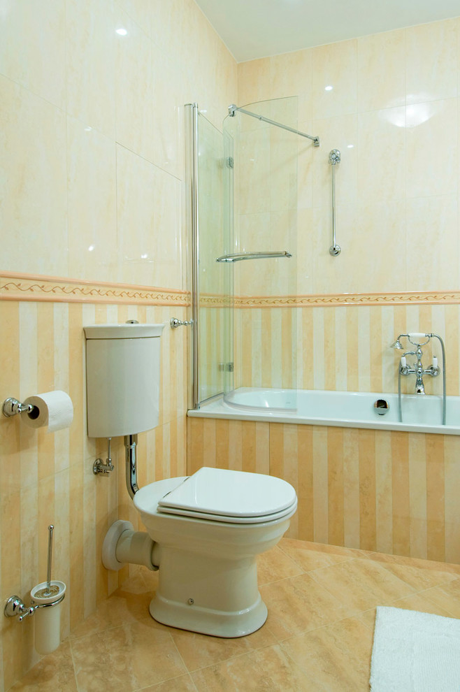 Bild på ett vintage badrum, med ett badkar i en alkov, en dusch/badkar-kombination, en toalettstol med separat cisternkåpa, beige kakel, gula väggar och med dusch som är öppen