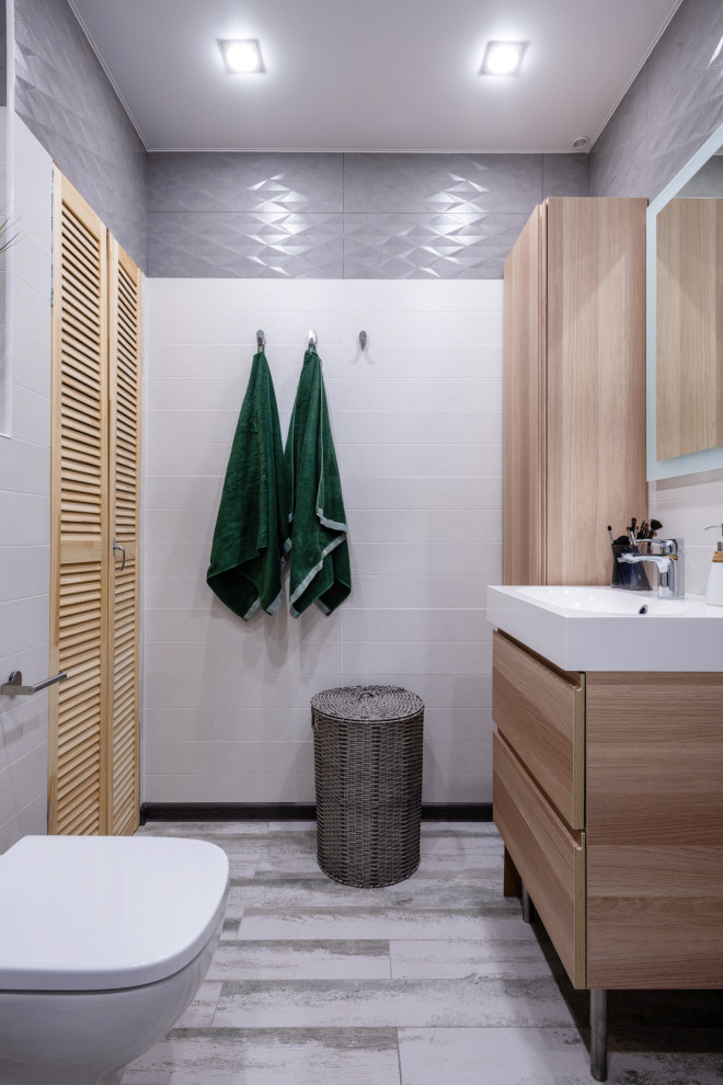 Cette image montre une petite salle de bain nordique en bois clair avec WC suspendus, un placard à porte plane, un carrelage blanc, un carrelage gris et un sol gris.