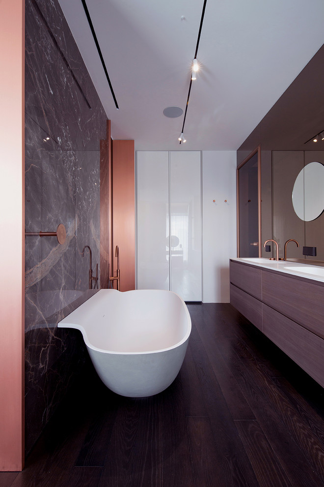 На фото: главная ванная комната в современном стиле с плоскими фасадами, фасадами цвета дерева среднего тона, отдельно стоящей ванной, белыми стенами, темным паркетным полом, монолитной раковиной, коричневым полом и белой столешницей