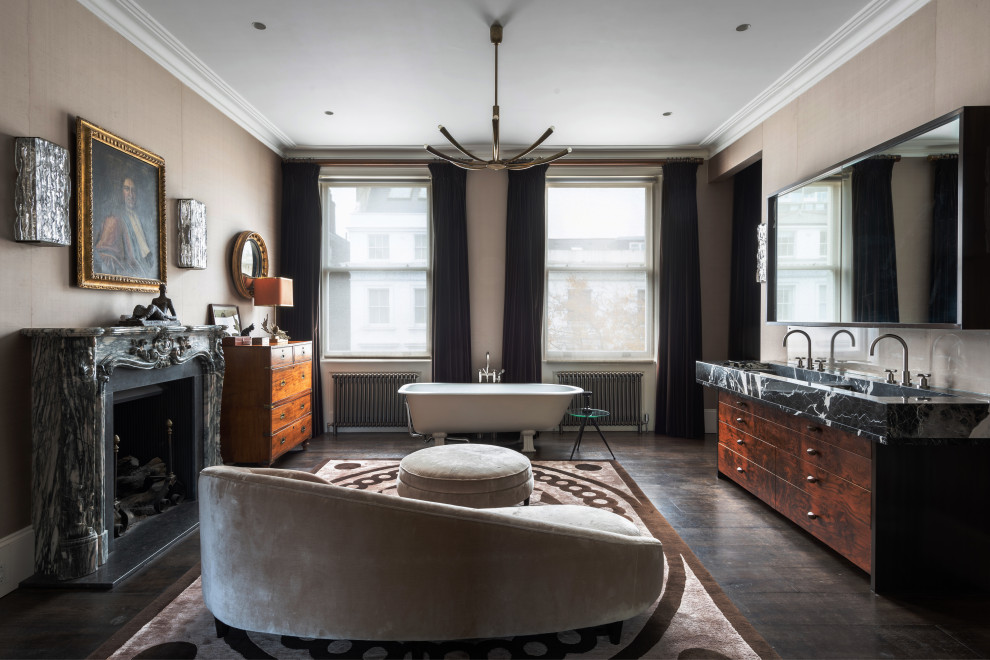 This is an example of a classic bathroom with flat-panel cabinets, dark wood cabinets, a claw-foot bath, beige walls, dark hardwood flooring, a trough sink, brown floors, black worktops and double sinks.