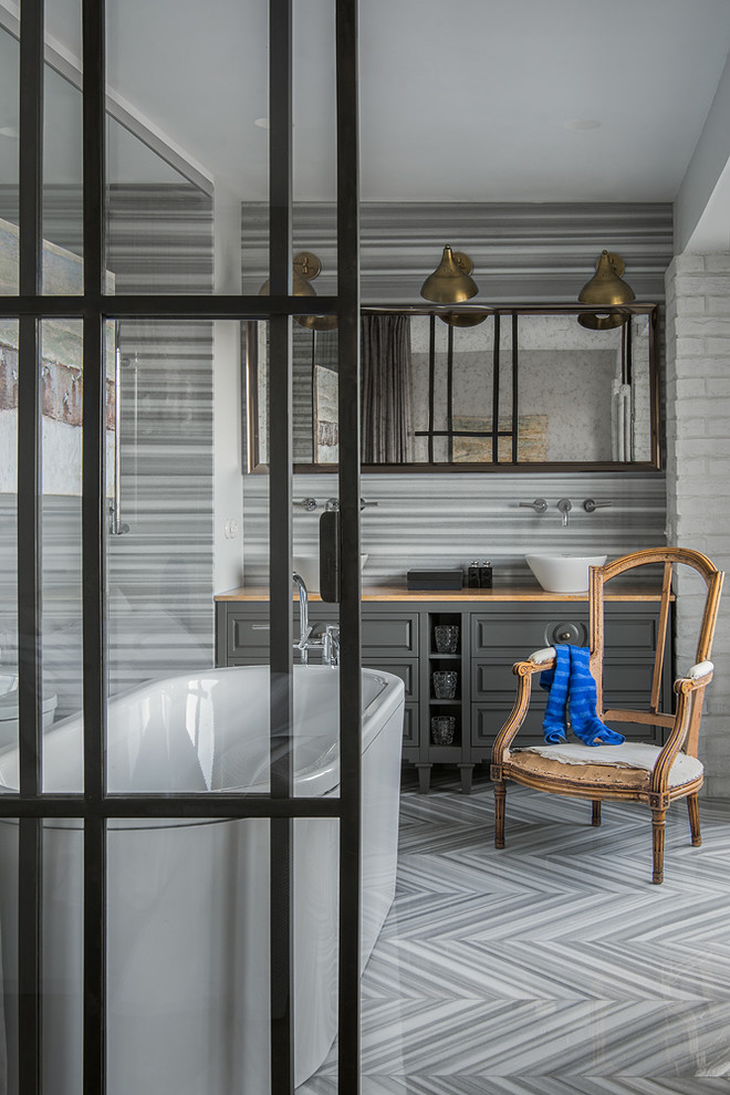 Пример оригинального дизайна: главная ванная комната в стиле неоклассика (современная классика) с серыми фасадами, отдельно стоящей ванной, настольной раковиной, серым полом и коричневой столешницей