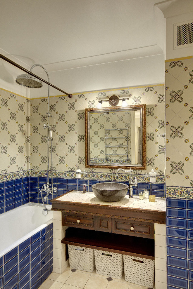 Inspiration for a traditional ensuite bathroom in Moscow with a shower/bath combination, blue tiles, metro tiles, a vessel sink, tiled worktops, medium wood cabinets, a built-in bath, multi-coloured walls and a shower curtain.