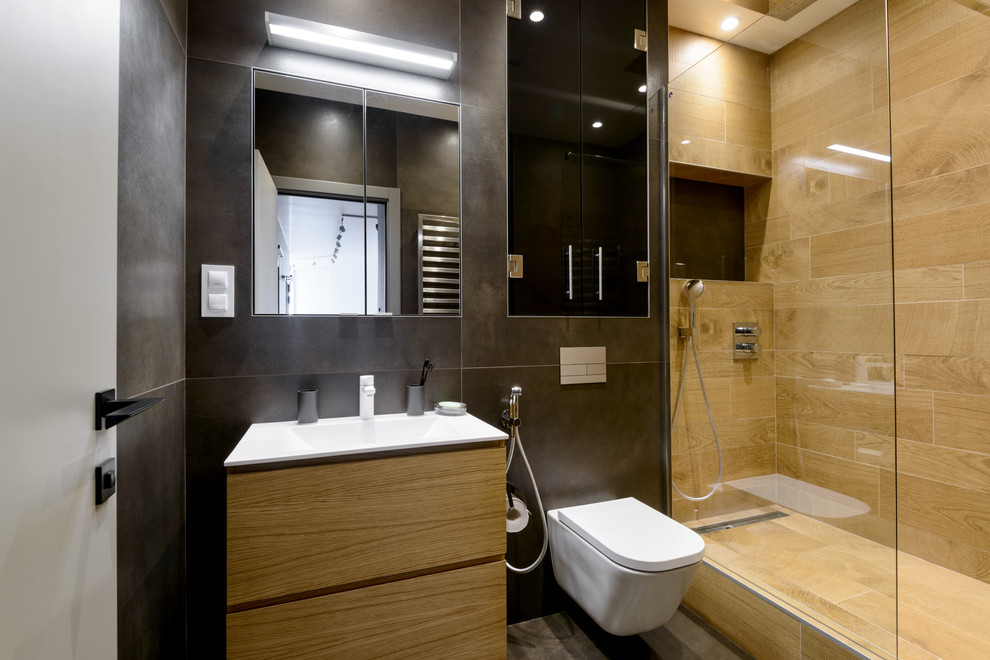 Modernes Duschbad mit flächenbündigen Schrankfronten, hellen Holzschränken, Duschnische, Wandtoilette, braunen Fliesen, Einbauwaschbecken und braunem Boden in Sonstige