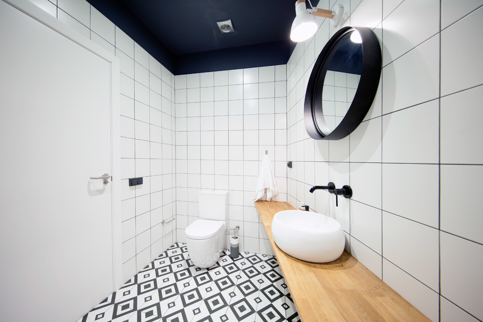 Foto på ett minimalistiskt beige badrum med dusch, med en toalettstol med separat cisternkåpa, vit kakel, ett fristående handfat, träbänkskiva och flerfärgat golv