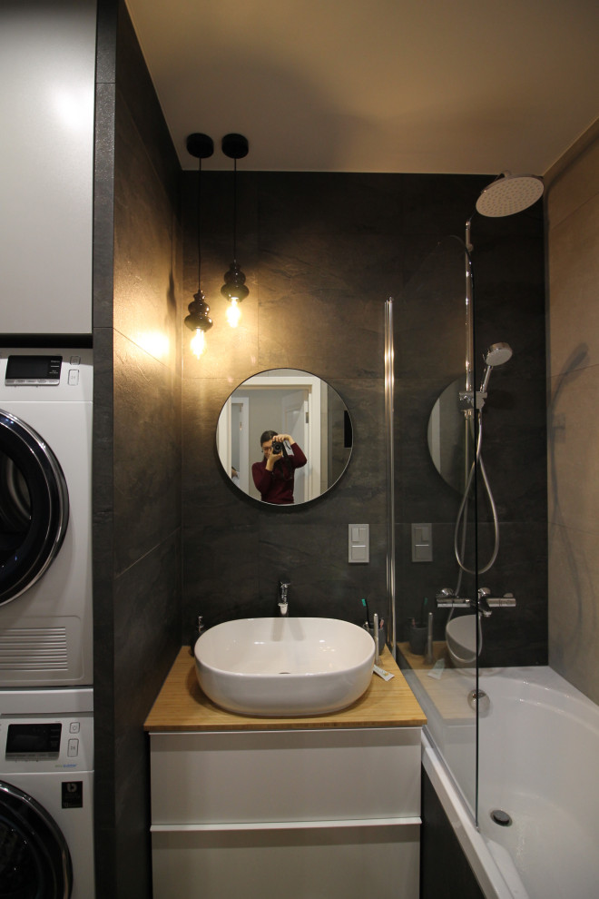 На фото: маленькая главная ванная комната со стиральной машиной в современном стиле с плоскими фасадами, полновстраиваемой ванной, душем над ванной, инсталляцией, черной плиткой, керамогранитной плиткой, серыми стенами, полом из керамогранита, накладной раковиной, столешницей из дерева, бежевым полом, шторкой для ванной, бежевой столешницей, тумбой под одну раковину и подвесной тумбой для на участке и в саду с