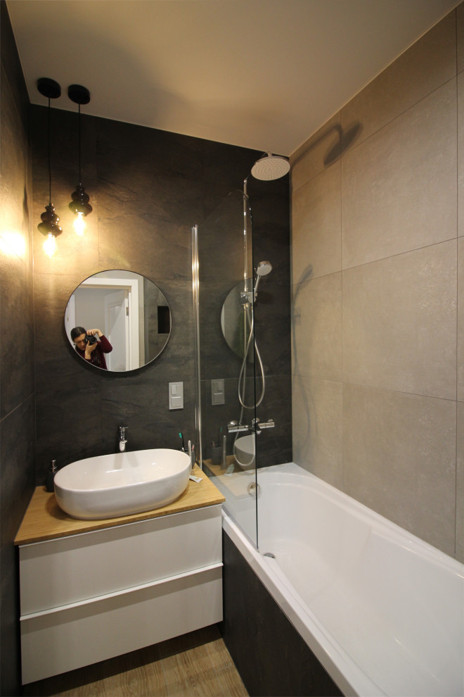 Источник вдохновения для домашнего уюта: маленькая главная ванная комната со стиральной машиной в современном стиле с плоскими фасадами, полновстраиваемой ванной, душем над ванной, инсталляцией, черной плиткой, керамогранитной плиткой, серыми стенами, полом из керамогранита, накладной раковиной, столешницей из дерева, бежевым полом, шторкой для ванной, бежевой столешницей, тумбой под одну раковину и подвесной тумбой для на участке и в саду