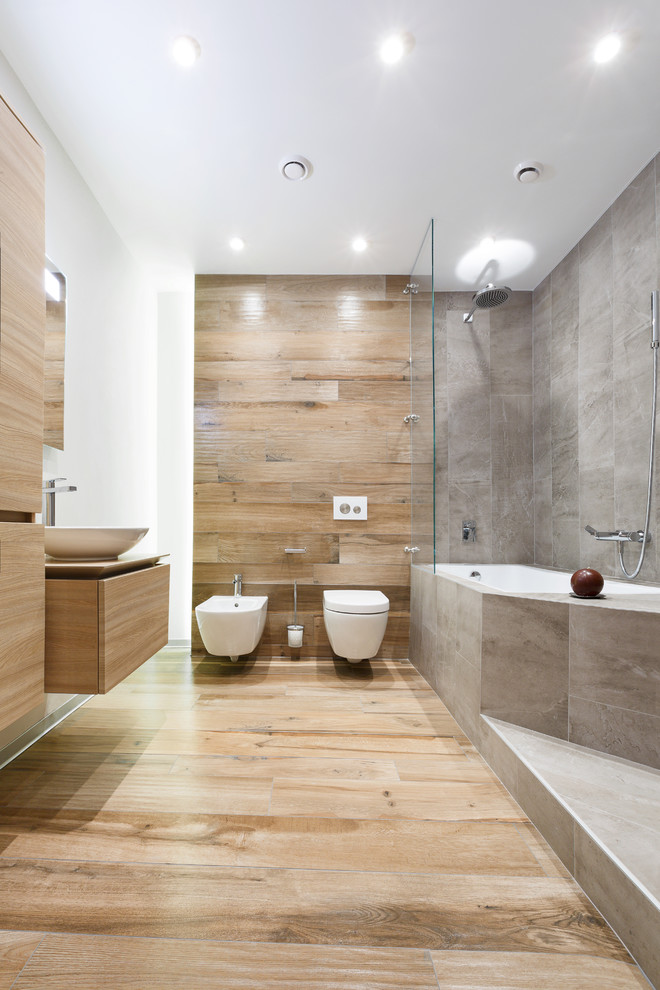 Esempio di una stanza da bagno padronale design di medie dimensioni con bidè, piastrelle grigie, piastrelle in gres porcellanato, pavimento in gres porcellanato, lavabo a bacinella, ante lisce, ante in legno chiaro, vasca da incasso e pavimento beige