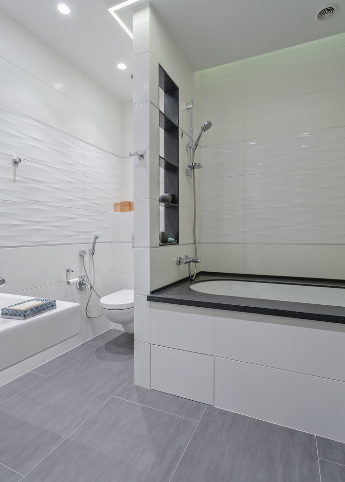 Diseño de cuarto de baño principal actual con bañera encastrada sin remate, combinación de ducha y bañera, sanitario de pared, baldosas y/o azulejos blancos y paredes blancas