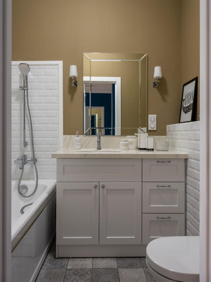 Cette image montre une salle de bain principale traditionnelle avec un placard à porte shaker, des portes de placard grises, une baignoire en alcôve, un combiné douche/baignoire, un carrelage blanc, un mur marron, un lavabo encastré, un sol gris, un plan de toilette beige, un carrelage métro et aucune cabine.