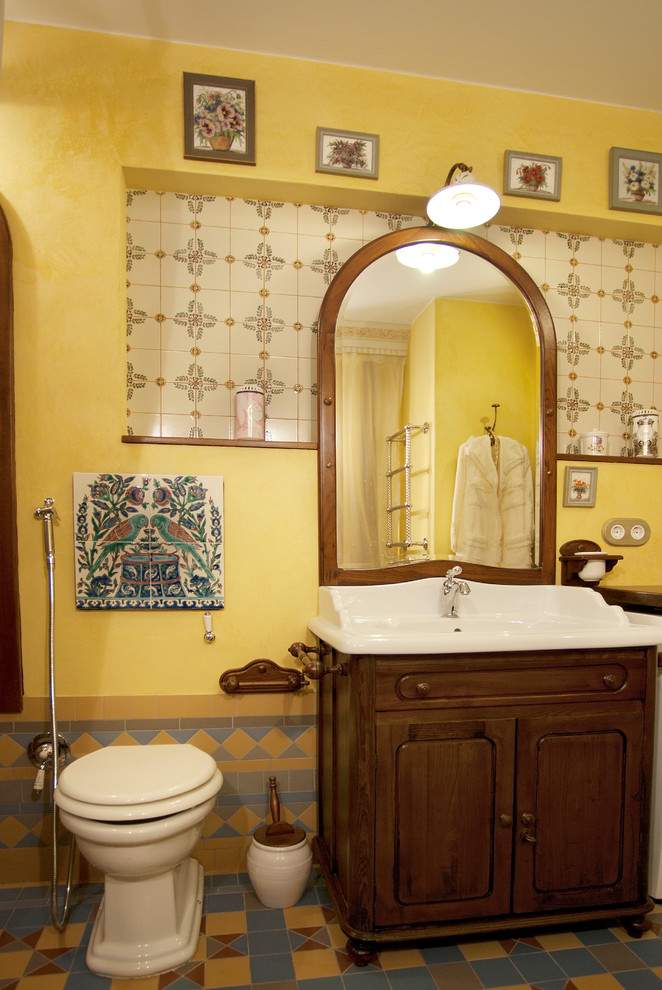 Пример оригинального дизайна: главная ванная комната среднего размера в стиле ретро с фасадами с утопленной филенкой, коричневыми фасадами, отдельно стоящей ванной, открытым душем, инсталляцией, разноцветной плиткой, керамической плиткой, желтыми стенами, полом из керамической плитки, монолитной раковиной, столешницей из ламината, разноцветным полом, шторкой для ванной, белой столешницей и акцентной стеной
