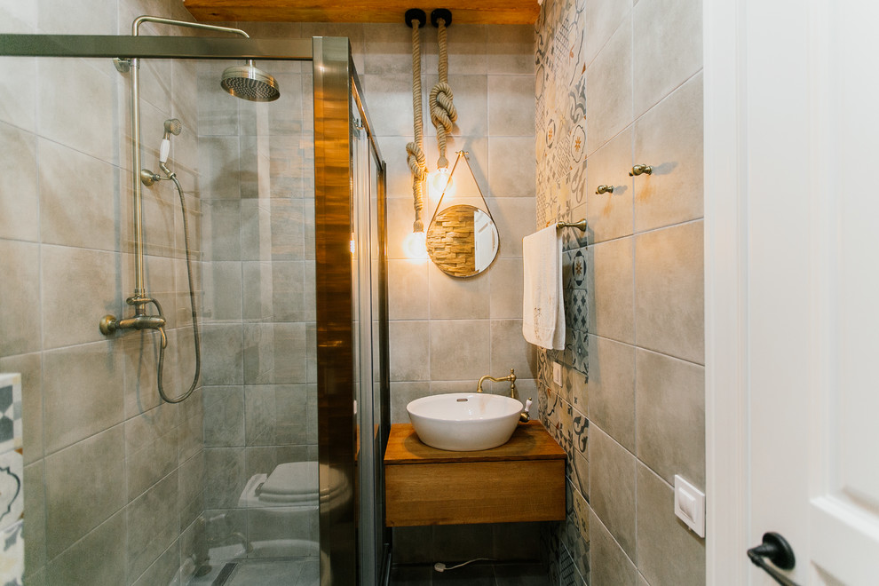 Cette image montre une salle d'eau méditerranéenne de taille moyenne avec une douche d'angle, WC suspendus, un carrelage gris, des carreaux de porcelaine, un mur gris, un sol en carrelage de porcelaine, une vasque, un plan de toilette en bois, un sol gris et une cabine de douche à porte coulissante.