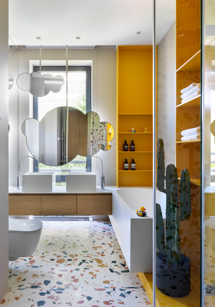 Cette photo montre une salle de bain grise et jaune tendance en bois brun avec un placard à porte plane, une baignoire d'angle, un mur blanc, un sol en terrazzo, une vasque, un sol multicolore et un plan de toilette blanc.