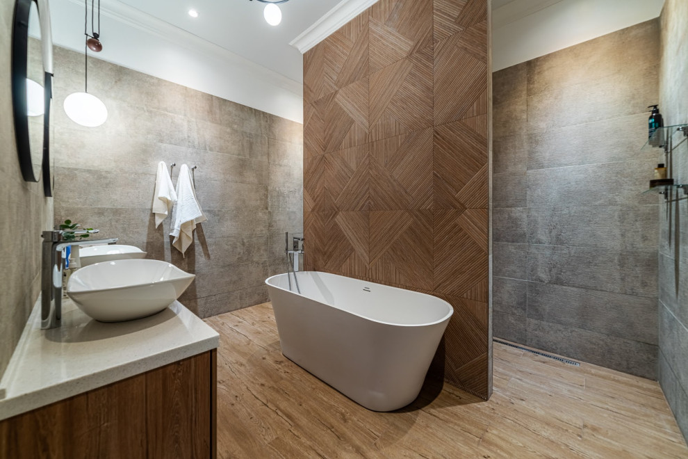 This is an example of a medium sized scandi ensuite bathroom in Saint Petersburg with flat-panel cabinets, brown cabinets, a freestanding bath, a shower/bath combination, a wall mounted toilet, grey tiles, porcelain tiles, brown walls, ceramic flooring, a vessel sink, solid surface worktops, brown floors, an open shower, grey worktops, an enclosed toilet, double sinks, a floating vanity unit, a drop ceiling and wainscoting.
