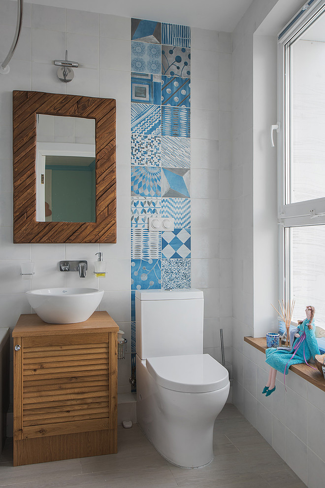 Maritimes Badezimmer mit Lamellenschränken, hellbraunen Holzschränken, Wandtoilette mit Spülkasten, blauen Fliesen, weißen Fliesen und Aufsatzwaschbecken in Moskau