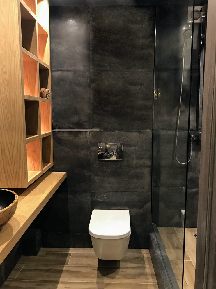 Foto på ett litet industriellt brun badrum med dusch, med en vägghängd toalettstol, svart kakel, svarta väggar, träbänkskiva, skåp i mellenmörkt trä, en hörndusch, ett fristående handfat, släta luckor, porslinskakel, brunt golv och dusch med duschdraperi