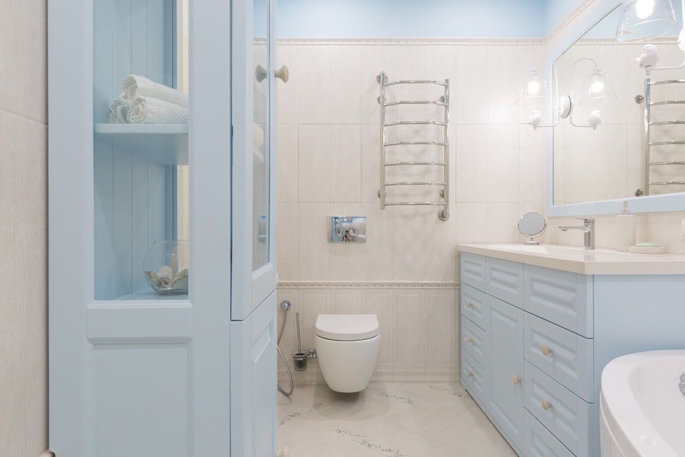 Klassisk inredning av ett mellanstort vit vitt en-suite badrum, med luckor med upphöjd panel, ett hörnbadkar, en dusch/badkar-kombination, en vägghängd toalettstol, beige kakel, stickkakel, beige väggar, klinkergolv i keramik, ett fristående handfat, bänkskiva i akrylsten, beiget golv och dusch med gångjärnsdörr