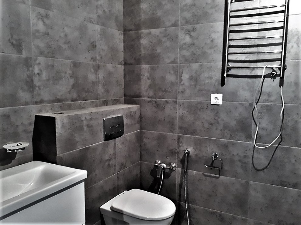 Minimalistisk inredning av ett badrum, med en vägghängd toalettstol, grå kakel, grå väggar, klinkergolv i keramik och grått golv