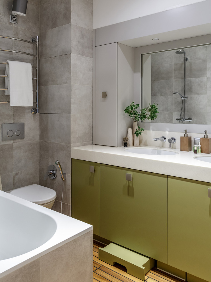 Cette photo montre une salle de bain principale tendance avec un placard à porte plane, des portes de placards vertess, une baignoire posée, WC suspendus, un carrelage gris, un mur gris et un lavabo encastré.