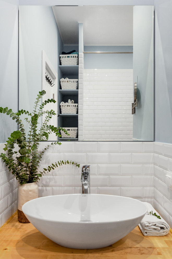 На фото: главная ванная комната в скандинавском стиле с полновстраиваемой ванной, душем над ванной, белой плиткой, керамогранитной плиткой, полом из керамогранита, накладной раковиной и столешницей из дерева с