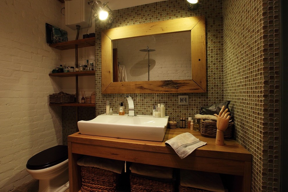 Cette image montre une petite salle d'eau urbaine avec mosaïque, une vasque, un plan de toilette en bois, WC séparés, un mur vert et un plan de toilette marron.