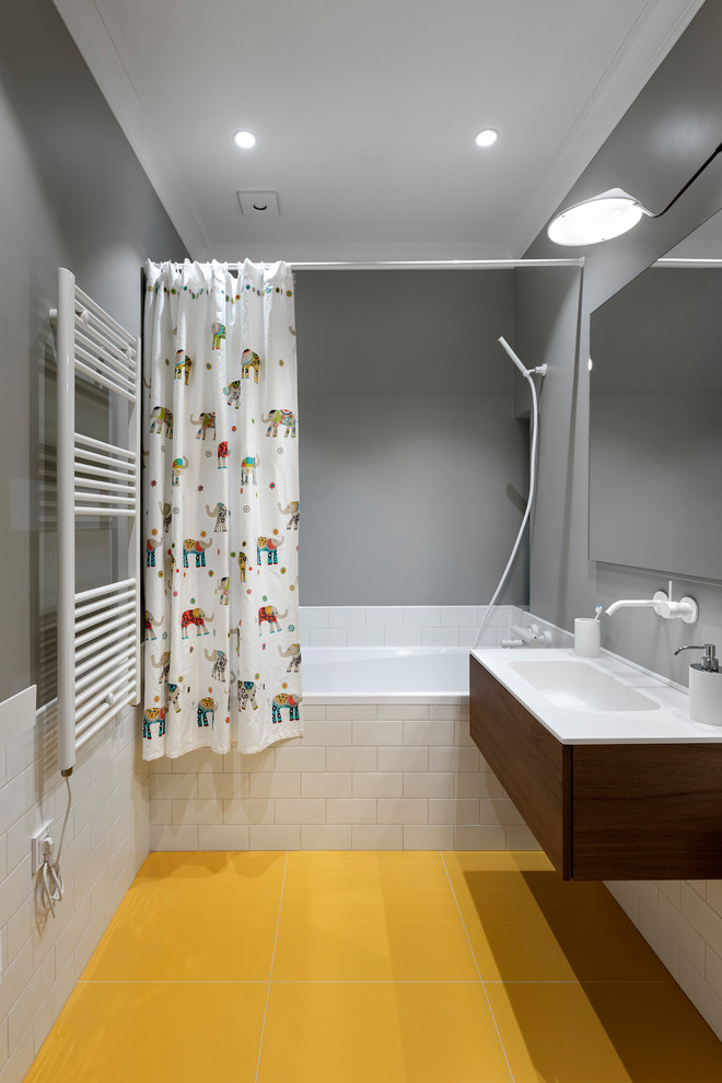 Свежая идея для дизайна: детская ванная комната в современном стиле с плоскими фасадами, темными деревянными фасадами, ванной в нише, душем над ванной, белой плиткой, плиткой кабанчик, серыми стенами, монолитной раковиной, желтым полом, шторкой для ванной и белой столешницей - отличное фото интерьера