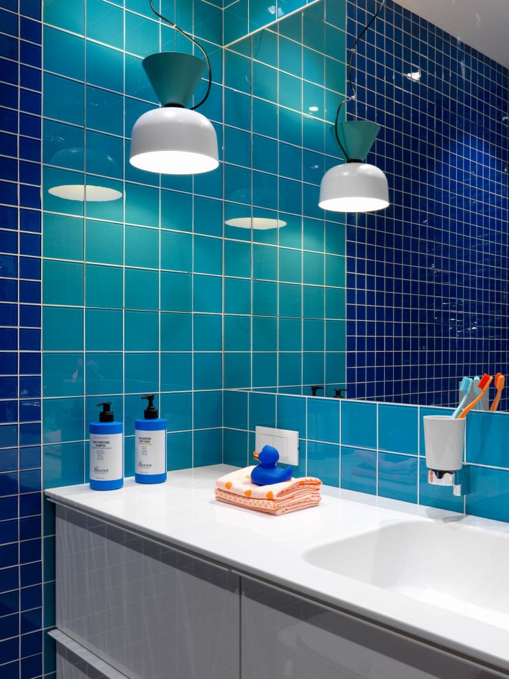 Idéer för att renovera ett mellanstort funkis vit vitt badrum med dusch, med släta luckor, vita skåp, en öppen dusch, en vägghängd toalettstol, orange kakel, glaskakel, blå väggar, klinkergolv i porslin, ett integrerad handfat, bänkskiva i akrylsten, grått golv och dusch med duschdraperi