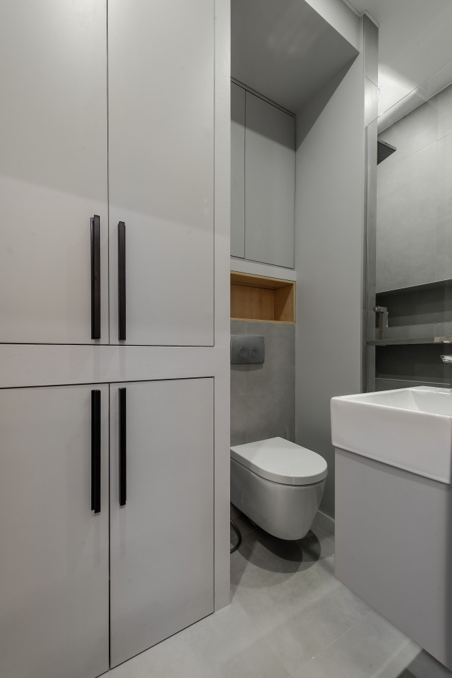 Idéer för att renovera ett funkis vit vitt badrum med dusch, med släta luckor, vita skåp, en dusch i en alkov, en vägghängd toalettstol, grå kakel, ett integrerad handfat och grått golv