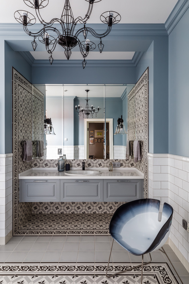 Klassisches Badezimmer mit profilierten Schrankfronten, grauen Schränken, farbigen Fliesen, weißen Fliesen, blauer Wandfarbe, Einbauwaschbecken, buntem Boden und weißer Waschtischplatte in Sonstige