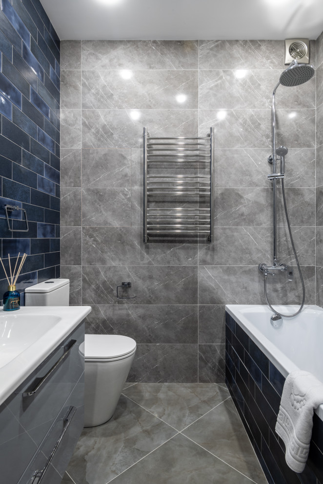 Exempel på ett litet modernt badrum, med grå skåp, ett undermonterat badkar, en toalettstol med hel cisternkåpa, blå kakel, keramikplattor, grå väggar, klinkergolv i porslin, ett integrerad handfat och grått golv