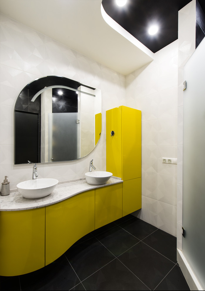 На фото: большая главная ванная комната в современном стиле с плоскими фасадами, желтыми фасадами, полновстраиваемой ванной, душевой комнатой, инсталляцией, черно-белой плиткой, керамической плиткой, черными стенами, полом из керамической плитки, настольной раковиной, столешницей из искусственного кварца, черным полом, душем с распашными дверями и белой столешницей