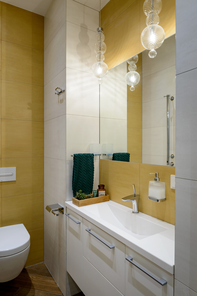 Пример оригинального дизайна: ванная комната в современном стиле с инсталляцией, столешницей из искусственного камня, плоскими фасадами, белыми фасадами, желтой плиткой, желтыми стенами, консольной раковиной, коричневым полом и белой столешницей