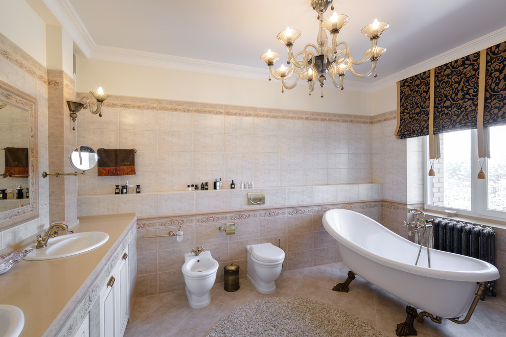 Стильный дизайн: большая главная ванная комната в классическом стиле с белыми фасадами, ванной на ножках, бежевой плиткой, керамической плиткой, бежевыми стенами, полом из керамической плитки, врезной раковиной и столешницей из искусственного камня - последний тренд