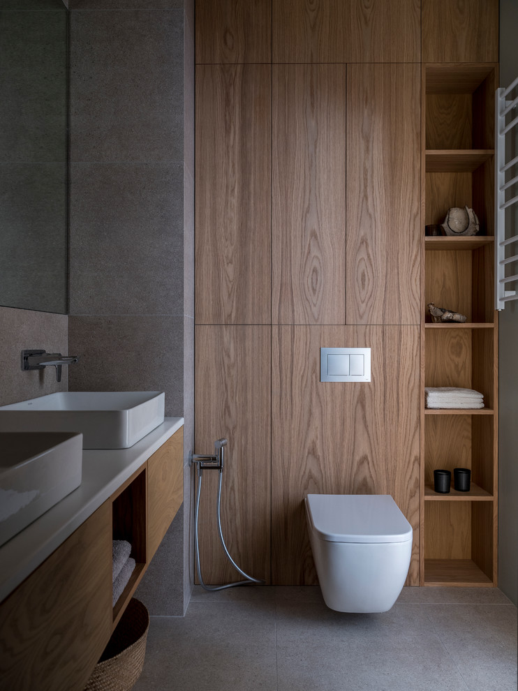 Cette photo montre une salle de bain tendance en bois brun avec un placard à porte plane, WC suspendus, un carrelage gris, une vasque, un sol gris et un plan de toilette blanc.