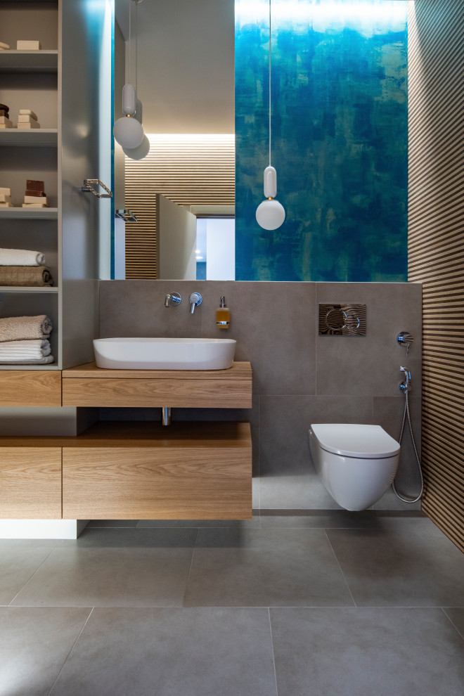 Идея дизайна: главная ванная комната среднего размера в современном стиле с плоскими фасадами, темными деревянными фасадами, отдельно стоящей ванной, душем над ванной, инсталляцией, бежевой плиткой, керамической плиткой, разноцветными стенами, полом из керамогранита, настольной раковиной, столешницей из дерева, серым полом, шторкой для ванной и бежевой столешницей